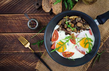Lezzetli kahvaltı. Yağda yumurta, orman mantarı, domates ve roka. Öğle yemeği. Üst görünüm, genel görünüm, kopyalama alanı