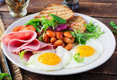 İngiliz kahvaltısı - kızarmış yumurta, fasulye, domates, sosis, jambon ve tost.