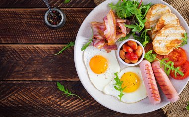 İngiliz kahvaltısı - kızarmış yumurta, fasulye, domates, sosis, pastırma ve tost. Üst görünüm, düz görünüm, genel görünüm
