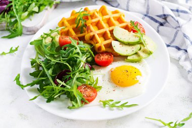 Beyaz arka planda kabaklı waffle, kızarmış yumurta, domates, avokado ve roka ile kahvaltı. Aperatifler, aperatifler, brunch. Sağlıklı vejetaryen yemekleri.