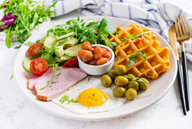 Kabak waffle 'lı kahvaltı, kızarmış yumurta, jambon, domates, avokado, fasulye ve beyaz arka planda zeytin. Aperatifler, aperatifler, brunch. Sağlıklı yemek..