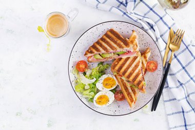 Jambon, domates, peynir, avokado ve bir fincan kahveyle ızgara sandviç sandviçi. Lezzetli kahvaltı ya da atıştırmalık. Üst manzara, düz uzanma