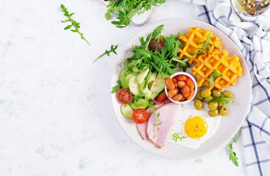 Kabak waffle 'lı kahvaltı, kızarmış yumurta, jambon, domates, avokado, fasulye ve beyaz arka planda zeytin. Aperatifler, aperatifler, brunch. Sağlıklı yiyecekler. Üst görünüm, genel görünüm, kopyalama alanı