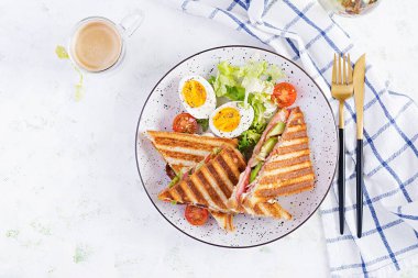 Jambon, domates, peynir, avokado ve bir fincan kahveyle ızgara sandviç sandviçi. Lezzetli kahvaltı ya da atıştırmalık. Üst manzara, düz uzanma