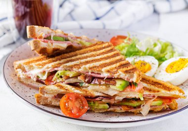 Jambon, domates, peynir, avokado ve bir fincan kahveyle ızgara sandviç sandviçi. Lezzetli kahvaltı ya da atıştırmalık.