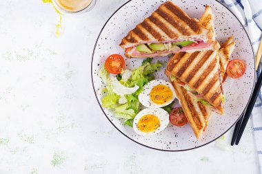 Jambon, domates, peynir, avokado ve bir fincan kahveyle ızgara sandviç sandviçi. Lezzetli kahvaltı ya da atıştırmalık. Üst manzara, düz uzanma