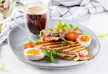 Jambon, domates, peynir, avokado ve bir fincan kahveyle ızgara sandviç sandviçi. Lezzetli kahvaltı ya da atıştırmalık.