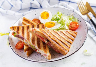 Jambon, domates, peynir, avokado ve bir fincan kahveyle ızgara sandviç sandviçi. Lezzetli kahvaltı ya da atıştırmalık.
