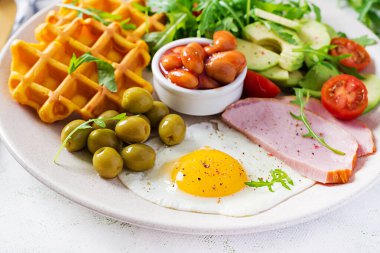 Kabak waffle 'lı kahvaltı, kızarmış yumurta, jambon, domates, avokado, fasulye ve beyaz arka planda zeytin. Aperatifler, aperatifler, brunch. Sağlıklı yemek..