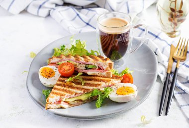 Jambon, domates, peynir, avokado ve bir fincan kahveyle ızgara sandviç sandviçi. Lezzetli kahvaltı ya da atıştırmalık.