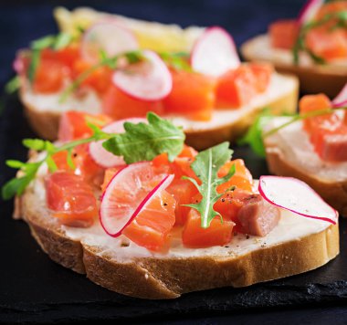 Sağlıklı kahvaltı için koyu arkaplanda tuzlu somonlu sandviç. Balık menüsü.