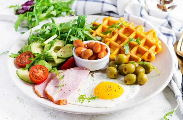 Kabak waffle 'lı kahvaltı, kızarmış yumurta, jambon, domates, avokado, fasulye ve beyaz arka planda zeytin. Aperatifler, aperatifler, brunch. Sağlıklı yemek..