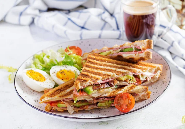 Jambon, domates, peynir, avokado ve bir fincan kahveyle ızgara sandviç sandviçi. Lezzetli kahvaltı ya da atıştırmalık.