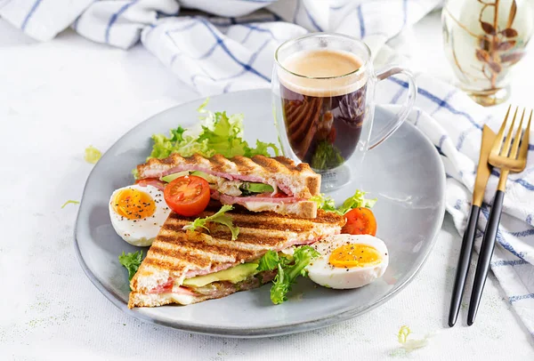 Jambon, domates, peynir, avokado ve bir fincan kahveyle ızgara sandviç sandviçi. Lezzetli kahvaltı ya da atıştırmalık.