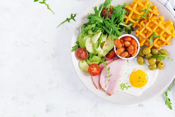Kabak waffle 'lı kahvaltı, kızarmış yumurta, jambon, domates, avokado, fasulye ve beyaz arka planda zeytin. Aperatifler, aperatifler, brunch. Sağlıklı yiyecekler. Üst görünüm, genel görünüm, kopyalama alanı