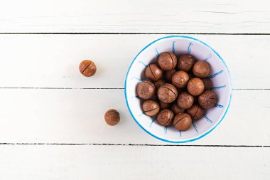 Tahta beyaz masa üzerinde organik Macadamia fındıkları (Macadamia integrifolia). Üst görünüm, genel görünüm, kopyalama alanı