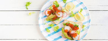 Somon kırmızısı havyarlı sandviç, dilimlenmiş avokado ve turp. Öğle yemeği için sandviç. Kaliteli yemek. Yukarıdan, yukarıdan, pankarttan