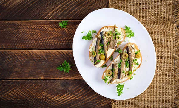 Sandwich - smorrebrod with sprats, green olives and butter on wooden table. Danish cuisine. Top view, overhead, flat lay — Stock Image Sandwich Smorrebrod Sprats Green Olives Butter Wooden Table Danish Cuisine Royalty Free Stock Images