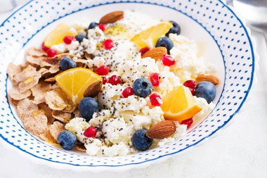 Bir kase gevrek, süzme peynir ve yoğurt, yaban mersini ve beyaz masada nar. Spor yemeği..