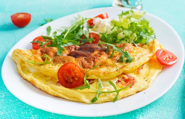 Kahvaltıda. Beyaz tabakta domatesli omlet, peynir ve roka. Frittata - İtalyan omleti. Ketogenik, keto yemeği..