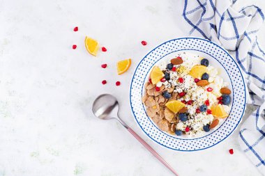 Bir kase gevrek, süzme peynir ve yoğurt, yaban mersini ve beyaz masada nar. Spor yemeği. Yukarıdan, yukarıdan, dümdüz.