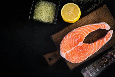 Somon balığı. Çiğ balık somon bifteği fileto, pişirme malzemeleri, otlar ve siyah arka planda limon ve fotokopi alanı. Üst görünüm, genel görünüm, kopyalama alanı.