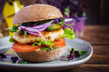 Hamburger. Tavuklu sandviç, domates, salatalık turşusu ve kırmızı soğanlı. Tahta masada taze tavuk burgeri..