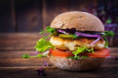 Hamburger. Tavuklu sandviç, domates, salatalık turşusu ve kırmızı soğanlı. Tahta masada taze tavuk burgeri..