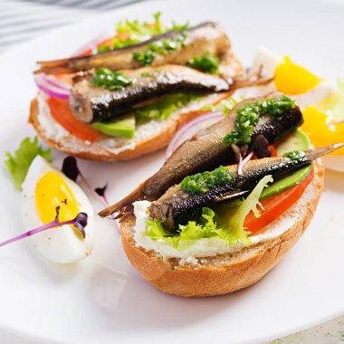 Sandviç, sprat, avokado, domates, yumurta ve krem peynirli beyaz tabak. Danimarka mutfağı. Çevre dostu kavram.