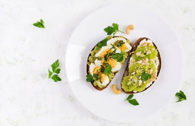 Vejetaryen kahvaltısı. Avokado püresi, haşlanmış yumurta, krem peynirli sandviç, kivi, fındık. Sağlıklı kahvaltı ya da öğle yemeği. Üst görünüm, genel görünüm