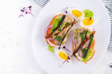 Sandviç, sprat, avokado, domates, yumurta ve krem peynirli beyaz tabak. Danimarka mutfağı. Üst manzara, genel giderler. Çevre dostu kavram.