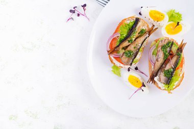 Sandviç, sprat, avokado, domates, yumurta ve krem peynirli beyaz tabak. Danimarka mutfağı. Üst manzara, genel giderler. Çevre dostu kavram.