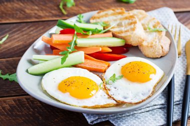 Kahvaltıda. Taze havuçlu yumurta, salatalık, kırmızı biber ve ahşap zemin üzerinde kızarmış ekmek. Vejetaryen yemeği.