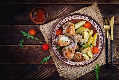 Fırında tavuk budu, patates dilimleri ve otlarla. Ahşap masada ızgara tavuk budu. Üst görünüm, genel görünüm, kopyalama alanı.