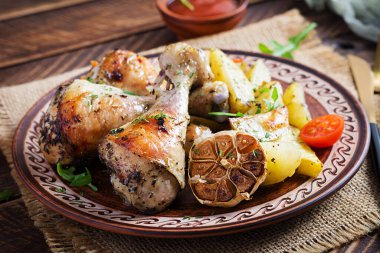 Fırında tavuk budu, patates dilimleri ve otlarla. Ahşap masada ızgara tavuk budu..