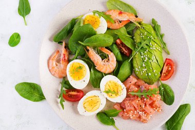 Ketogenik diyet kahvaltısı. Haşlanmış karides, karides, domates, ıspanak, yumurta ve avokado ile tuzlu somon salatası. Keto, paleo yemeği. Üst görünüm, genel görünüm