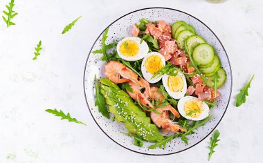 Ketogenik diyet kahvaltısı. Haşlanmış karides, karides, salatalık, roka, yumurta ve avokado ile tuzlu somon salatası. Keto, paleo yemeği. Üst görünüm, genel görünüm