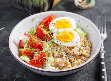 Kahvaltı yulaf lapası haşlanmış yumurta, kiraz domatesleri, kereviz ve mikro yeşillikler. Sağlıklı dengeli yiyecekler.