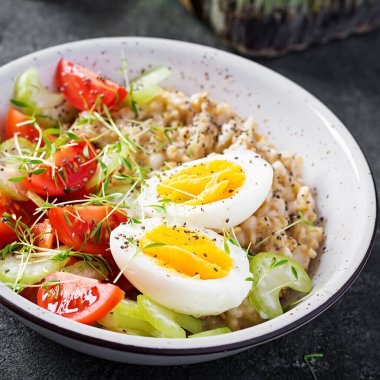 Kahvaltı yulaf lapası haşlanmış yumurta, kiraz domatesleri, kereviz ve mikro yeşillikler. Sağlıklı dengeli yiyecekler.