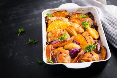 Fırında tavuk butları. Pişmiş tavuğun iştah açıcı dilimleri kırmızı soğanlı ve portakallı fırın kabında..