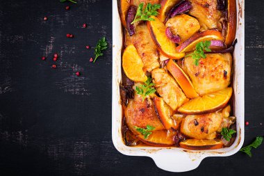 Fırında tavuk butları. Fırında pişmiş tavuğun iştah açıcı dilimleri, kırmızı soğan ve portakallı fırın kabında. Üst görünüm, alanı kopyala