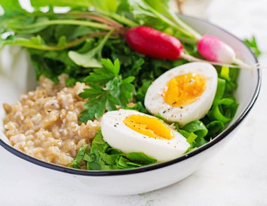 Kahvaltı yulaf lapası, haşlanmış yumurta, turp ve yeşil otlar. Sağlıklı dengeli yiyecekler.