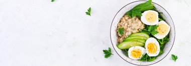 Kahvaltı yulaf lapası, haşlanmış yumurta, salatalık ve yeşil otlar. Sağlıklı dengeli yiyecekler. Üst görünüm, yukarıda, afiş