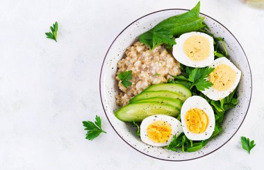 Kahvaltı yulaf lapası, haşlanmış yumurta, salatalık ve yeşil otlar. Sağlıklı dengeli yiyecekler. Üst görünüm, yukarıda
