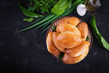 Geleneksel Ukrayna turtaları, yumurtalı, yeşil soğanlı, koyu arkaplanlı. Rus piroshki, ev yapımı fırında köfte. Üst görünüm, yukarıda, boşluğu kopyala