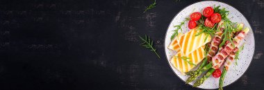 Izgara Halloumi peynirli salata, domatesli ve kuşkonmaz, koyu arkaplanda domuz pastırması şeritli. Sağlıklı yiyecekler. Üst görünüm, yukarıda
