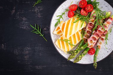 Izgara Halloumi peynirli salata, domatesli ve kuşkonmaz, koyu arkaplanda domuz pastırması şeritli. Sağlıklı yiyecekler. Üst görünüm, yukarıda