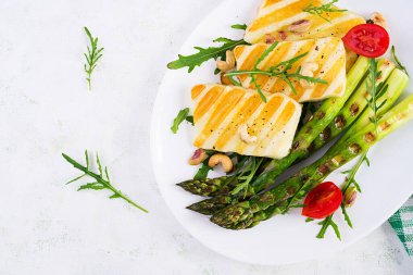 Izgara halloumi peynirli salata, domatesli ve hafif arka planda kuşkonmaz. Sağlıklı vejetaryen yemekleri. Üst görünüm