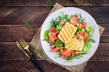 Izgara Halloumi peynirli salata, tuzlu somon, domates ve yeşil otlar. Ahşap arka planda tabakta sağlıklı yemek. Üst görünüm, yukarıda