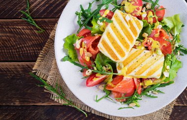 Izgara Halloumi peynirli salata, tuzlu somon, domates ve yeşil otlar. Ahşap arka planda tabakta sağlıklı yemek. Üst görünüm, afiş